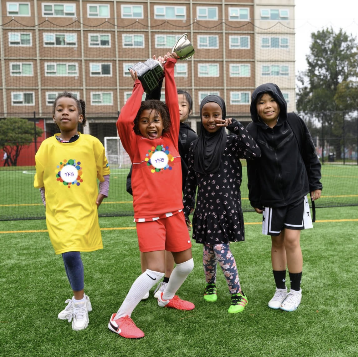 Four young players celebrating together on the pitch beside the Richmond housing estate